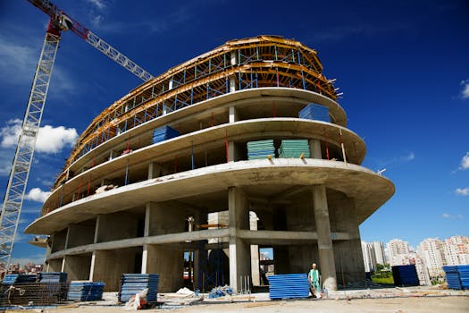 Low angle view of a circular building under construction with a crane, clear blue sky.